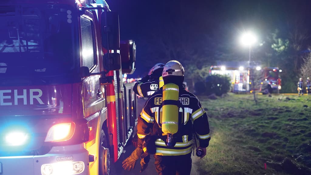 Feuerwehr bei einem Einsatz neben dem Feuerwehr-Fahrzeug